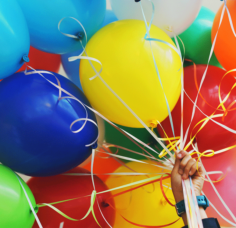 Kolorowe balony na sznurkach trzymane przez mężczyznę.