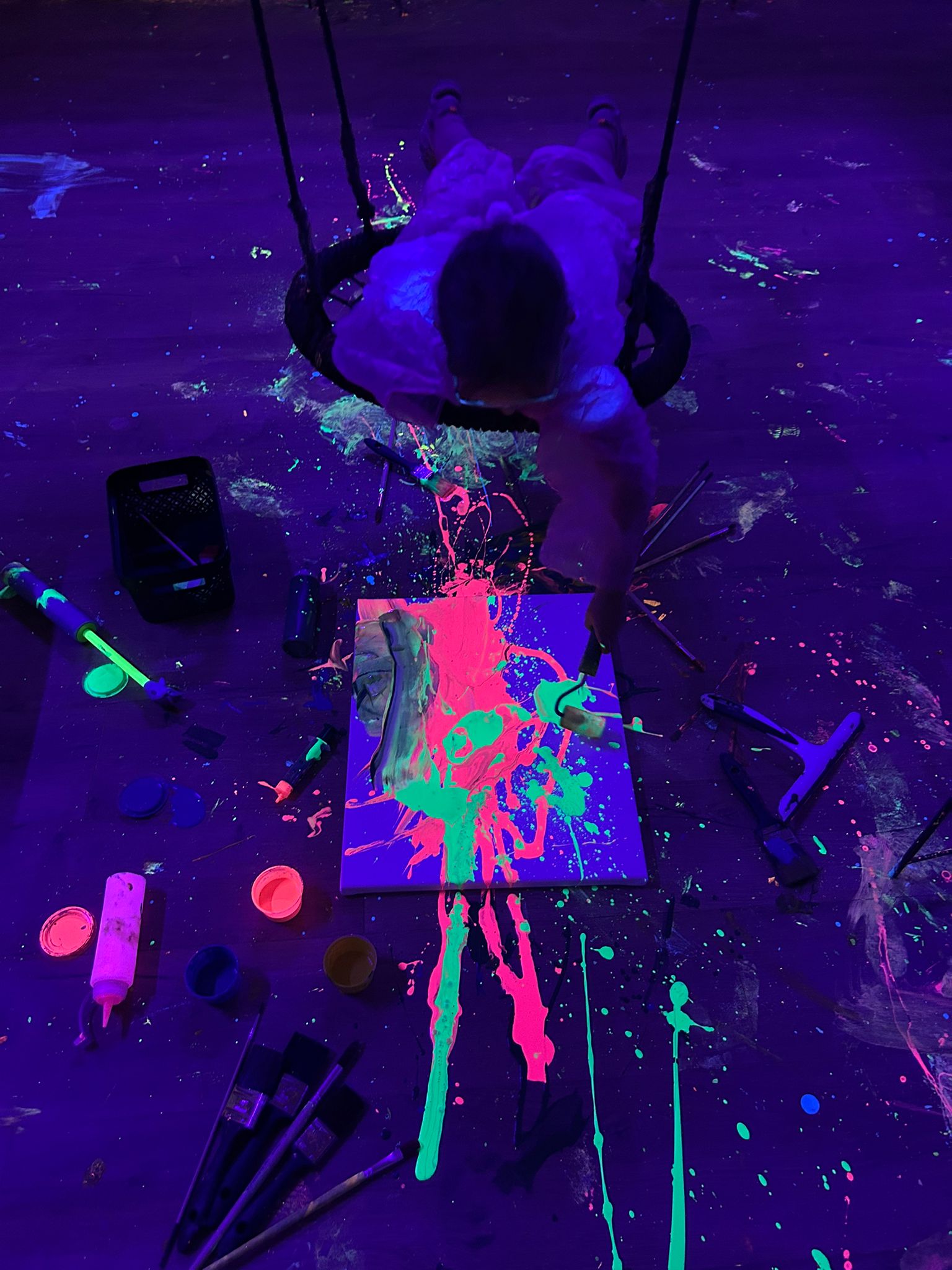Dziecko maluje fluorescencyjnymi farbami huśtając się na huśtawce.