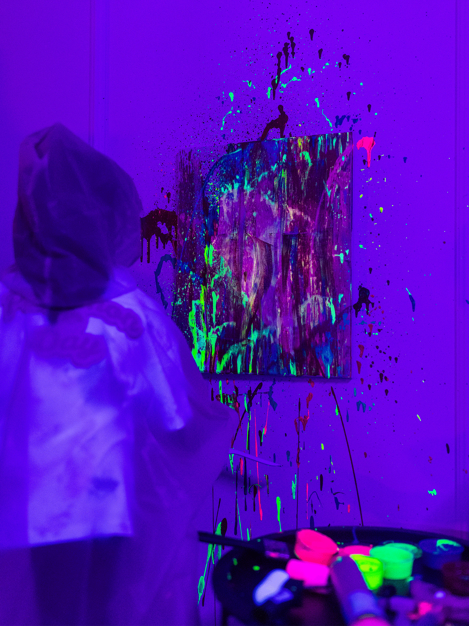 Dziecko maluje obraz chlapiąc farbami fluorescencyjnymi.