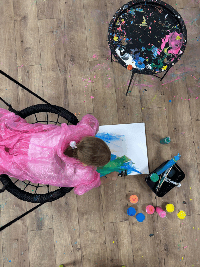 Dziecko leży na huśtawce i maluje obraz.